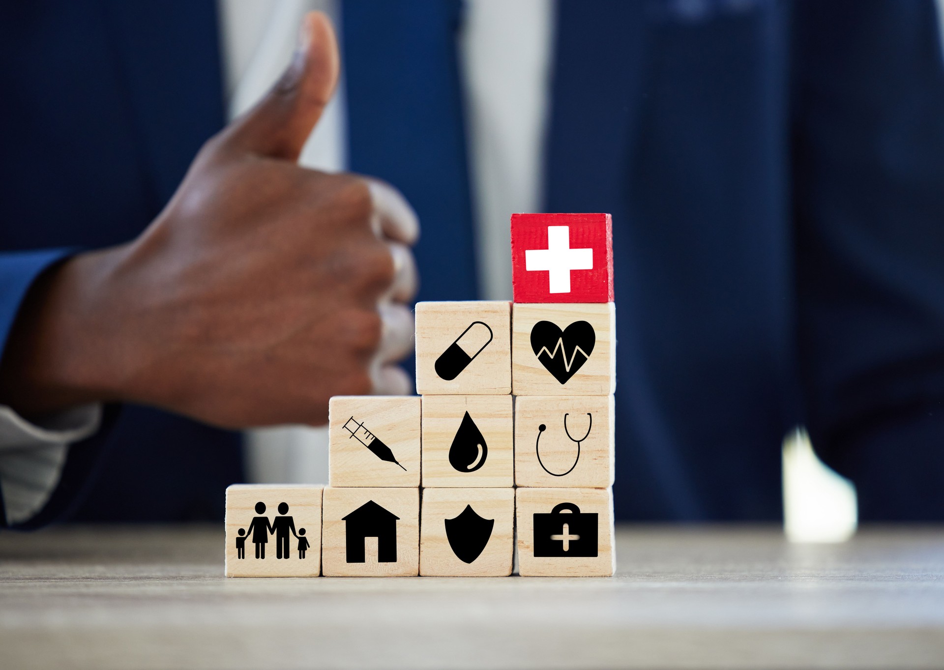 Shot of an unrecognisable businessman assembling wooden blocks with insurance related symbols on them and showing thumbs up